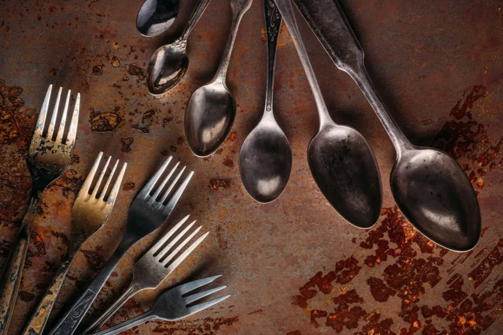 A collection of vintage forks and spoons arranged on a textured, rust-colored background, showcasing their unique patina.