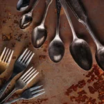 A collection of vintage forks and spoons arranged on a textured, rust-colored background, showcasing their unique patina.