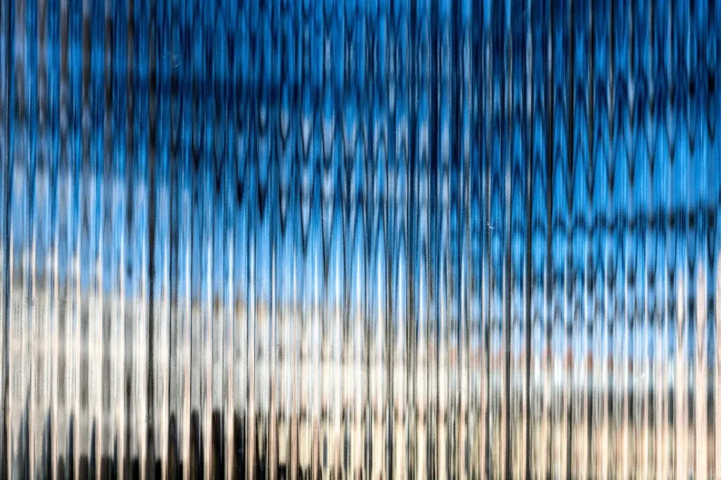 A blurred reflection of a bright blue sky and clouds creates a wavy, textured pattern, enhancing the sense of depth.