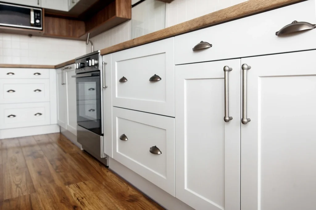 A modern kitchen with white cabinets, stainless steel appliances, and wooden countertops, featuring sleek hardware and warm wood floors.