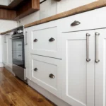 A modern kitchen with white cabinets, stainless steel appliances, and wooden countertops, featuring sleek hardware and warm wood floors.