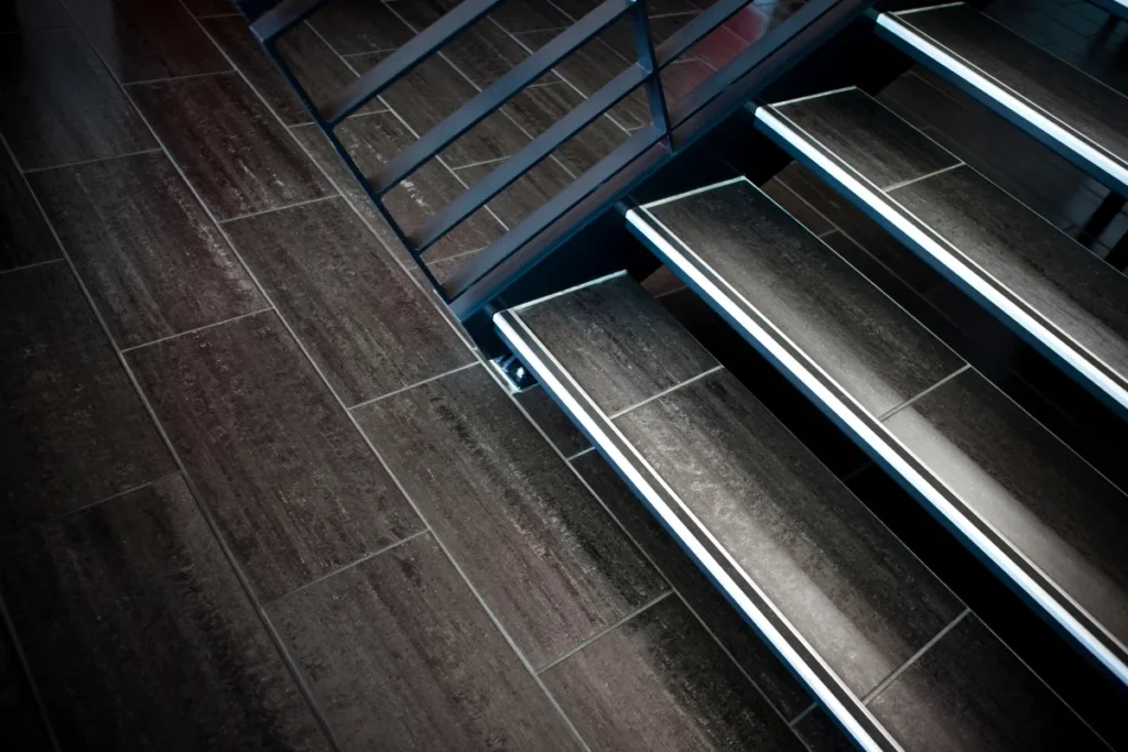 Close-up view of modern indoor stairs with dark stair treads and a metal railing, shot at an angle showing the steps and part of the adjacent tiled floor.