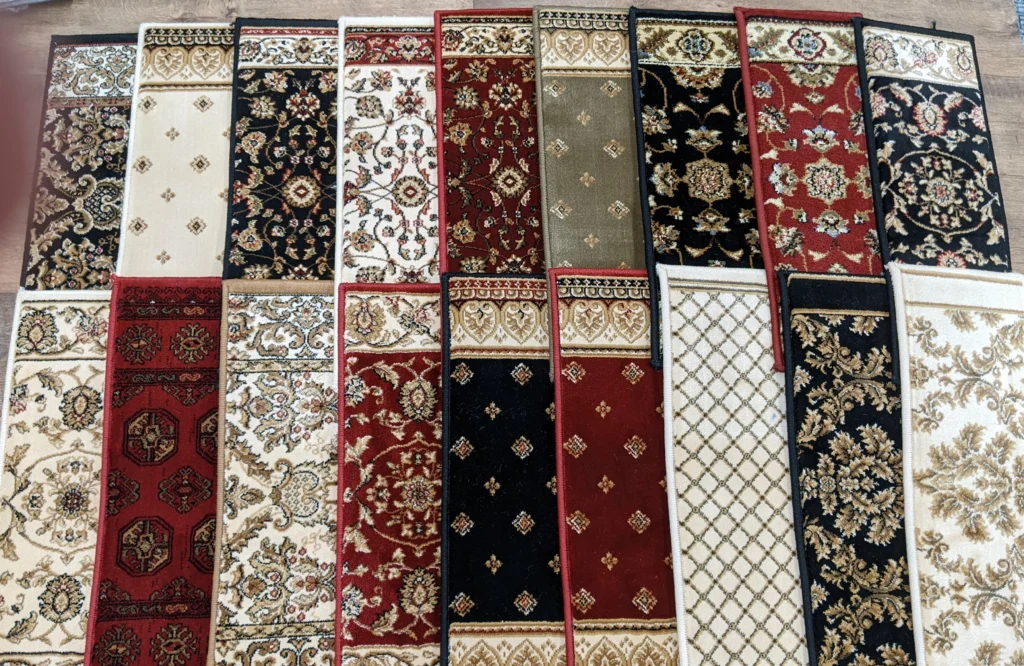 Five pairs of rectangular rugs in red, black, beige, and green hues with floral and geometric patterns are displayed on a wooden floor.
