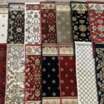 Five pairs of rectangular rugs in red, black, beige, and green hues with floral and geometric patterns are displayed on a wooden floor.
