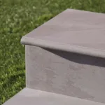 Close-up of smooth gray stone steps with rounded edges next to neatly trimmed green grass.