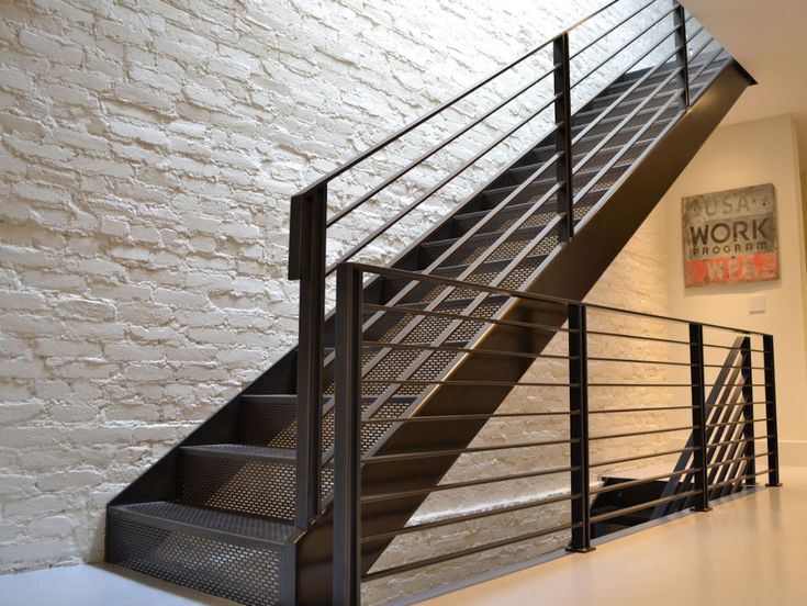 Modern black metal staircase with perforated steps and railings against a white brick wall in a minimalist interior.