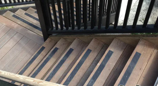 Wooden outdoor stairs with black anti-slip strips, bordered by black vertical railing, descending beside a deck.
